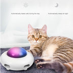 Cat interacting with a pet toy that changes color between purple and blue, with text indicating it automatically teases during the day and sleeps at night.