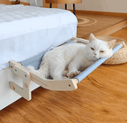 White cat lounging on a wooden cat hammock in a bedroom.