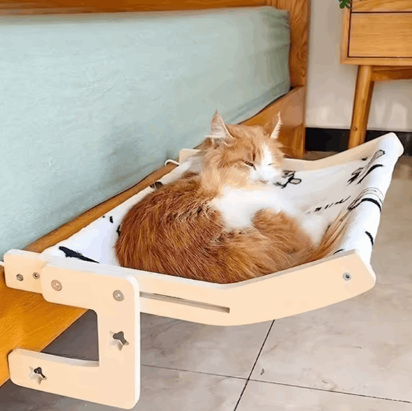 Cat lounging on a wooden cat hammock with a white cushion in a home setting.